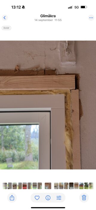 Nytt fönster med runtliggande isolering och trä i en gammal stuga. Synliga hål i väggen ovanför fönstret där gammalt material sitter kvar.