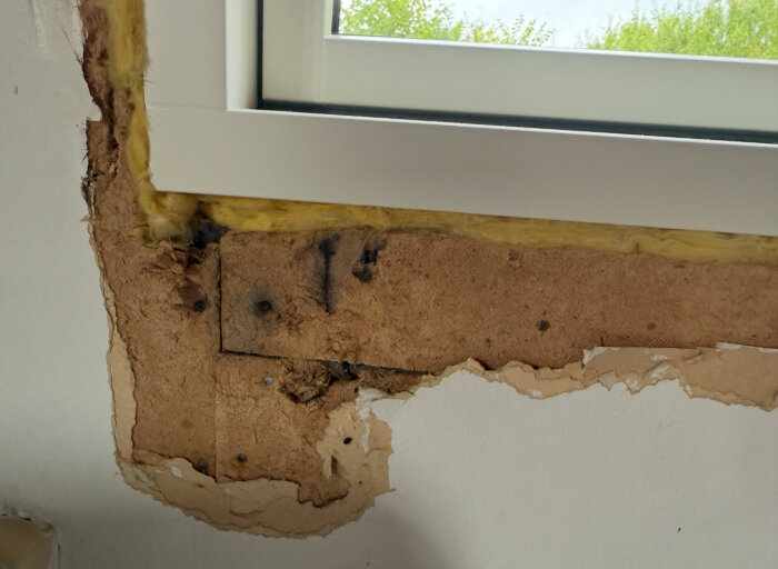 Nytt fönster med hål i väggen runt om, gamla isoleringsskivor och papp synliga i en stuga byggd 1934.