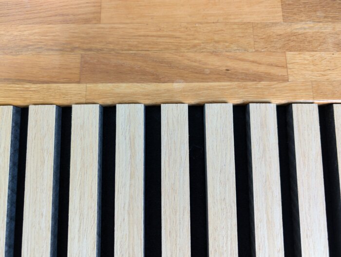 Ljus träakustikpanel med svart bakgrund, placerad på en ekbänkskiva.