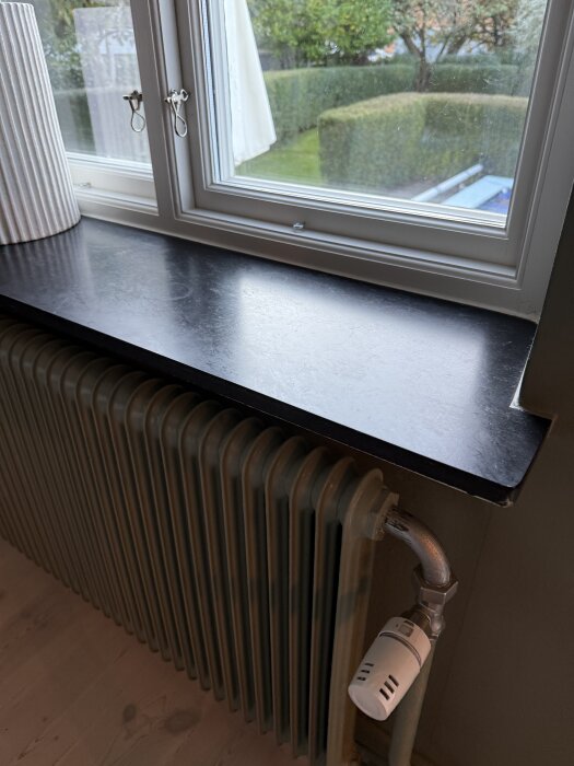 Radiator under fönsterbräda med utsikt över trädgård.