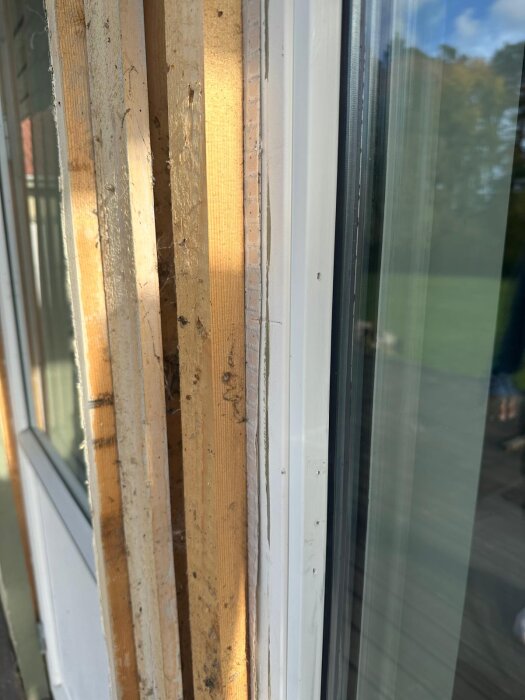 Närbild av ett fönster med glas intill flera lager av trä och isolering under en renovering, utomhusmiljö i bakgrunden.