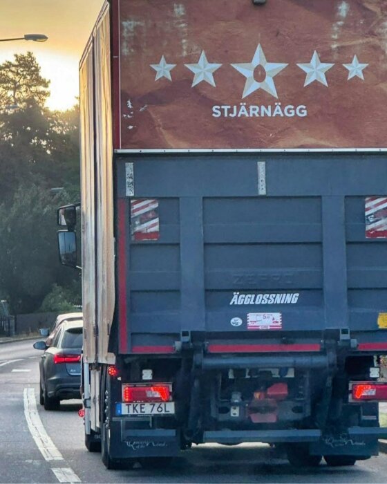 Lastbil med skylt "STJÄRNÄGG" och text "ÄGGLOSSNING" på bakdörren, kör på väg med bil bakom vid solnedgång.