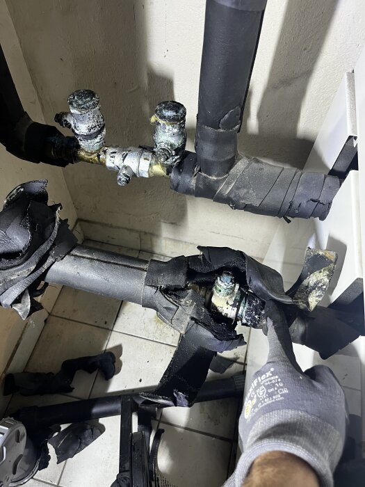 VVS-rör med ventiler och isolering, en hand i handske pekar vid ventilerna.