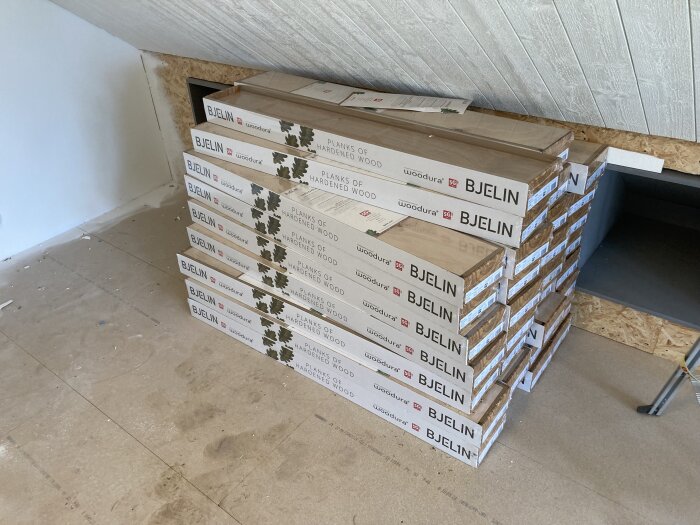 Staplade paket med Bjelin golvplankor i ett rum under renovering, delvis ohyvlade ytor syns.