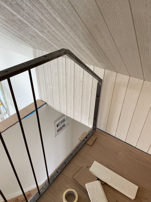 Metallräcke på ett loft med träpaneler och golv i ljus ton, omgärdat av verktyg och materialrester.