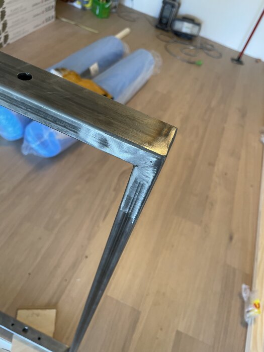 Svetsad metallkonstruktion på trägolv med verktyg och material i bakgrunden.