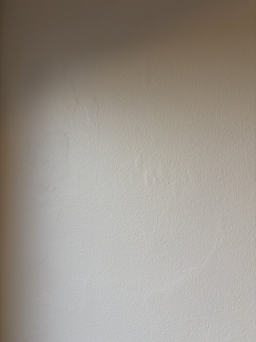 Ojämn vitmålad vägg med synliga tapetrester och spacklotsar. Resultatet efter dåligt utfört förarbete och slipning diskuteras.