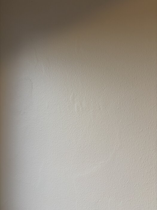 Ojämn, målad vägg med tydliga texturer och skuggor, troligen på grund av bristande grundarbete och slipning.