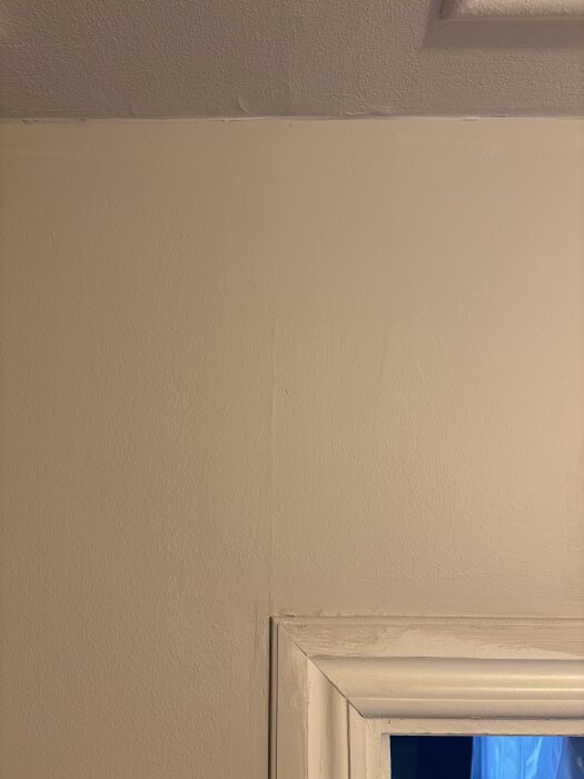 Ojämn målning och spackling på vägg nära tak, med synliga märken och skuggor orsakat av otillräckligt förarbete och slipning av underlaget.