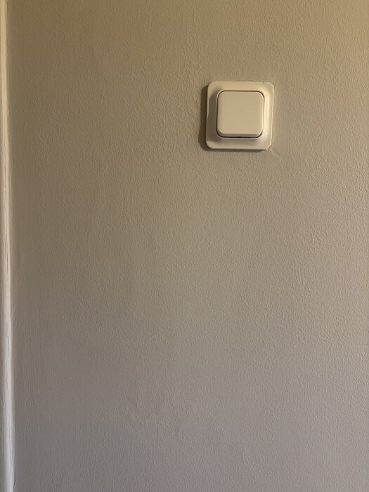 Oregelbundet målad vägg med ljus strömbrytare, tydliga ojämnheter syns på ytan.