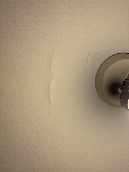 Ojämn och slarvigt målad vägg bredvid en taklampa, synliga skarvar och bristfälligt förarbete vid renovering.