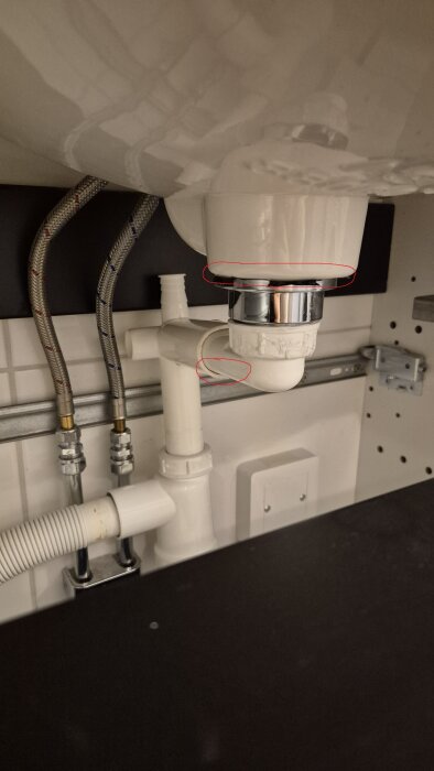 Handfatets avlopp under diskbänken med två röda cirklar markerar läckande områden, inklusive kopplingar och vattenlås.