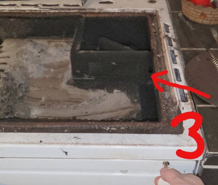 Öppen asklåda med vit aska, nummer 3 pekar på ett startspjäll styrt av ett handtag, omgivet av ett gammalt, rostigt ramverk.