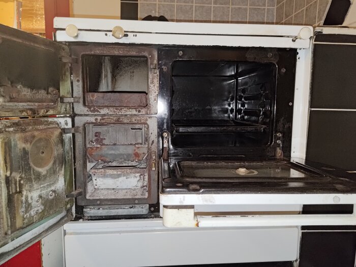 Gammal vedspis med öppnade luckor. Inre utrymmena synliga, vissa delar rostiga och sotiga. Möjlig asklåda och ugnsdel visas.