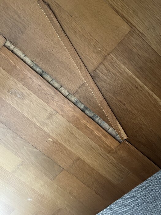 Skadat trägolv med lossat och sprucket fanér efter läckage från en portabel AC.