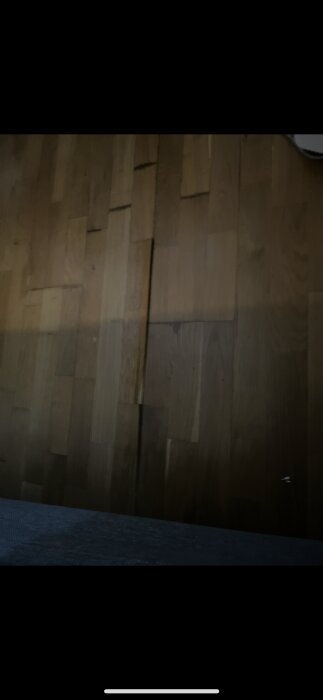 Skadat trägolv med lossnade faner, orsakat av läckande portabel AC. Golvbräda synligt sprucken i närbild.