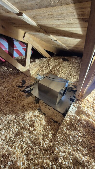Vind med isolering och en nyinstallerad fläkt, omgivet av sågspån och takbjälkar.