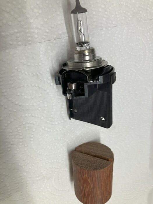 Glödlampahållare med vingar och ett handgjort verktyg av trä för byte av halvljus på bil. Verktyget har en skåra för grepp.