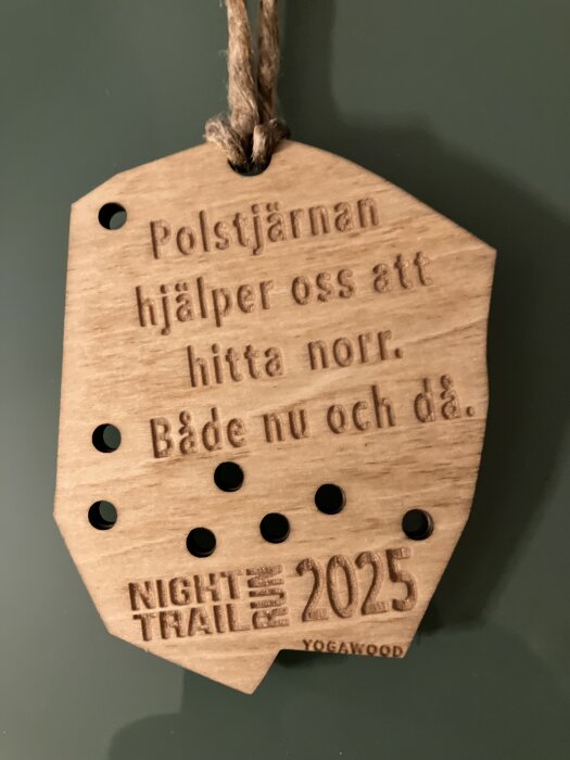 Träskylt med text om Polstjärnan som hjälpmedel för att hitta norr. Skylten har hål och texten "Night Trail Run 2025" samt "Yogawood".