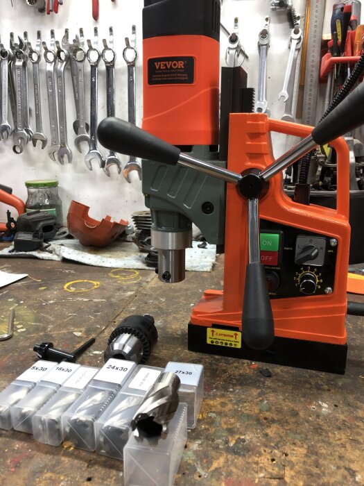 Borrmaskin och olika borrhuvuden i verkstadsmiljö med upphängda skiftnycklar i bakgrunden.