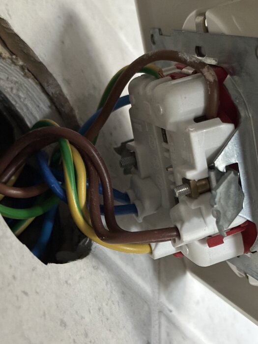 Närbild av ett eluttag i ett kök med flera kablar kopplade till faser, jord och nolla, del av ett installationsprojekt för byte till fyrabrunnarsuttag.