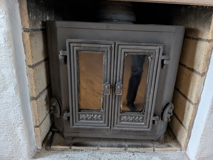 Kamin med två glasluckor, inramad av tegelväggar. En reflektion av en person syns i glaset.