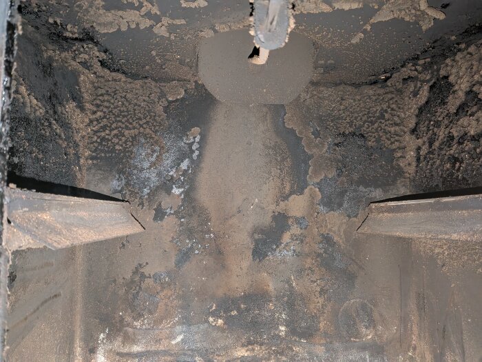 Närbild av insidan på en sotig Roslagsspis med metallväggar, tydligt spår av användning och sotavlagringar.