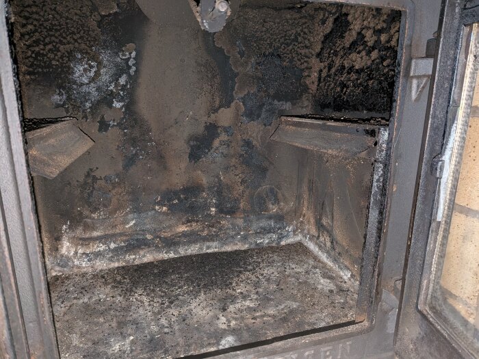 Insidan av en sotad Roslagsspis med öppna luckor, belagd med sot och aska.