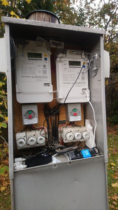 Elskåp med två elmätare från Vattenfall, inkopplade med kablar och omgivna av träd. En RJ12-kabel och svart antenn är ansluten till den högra mätaren.