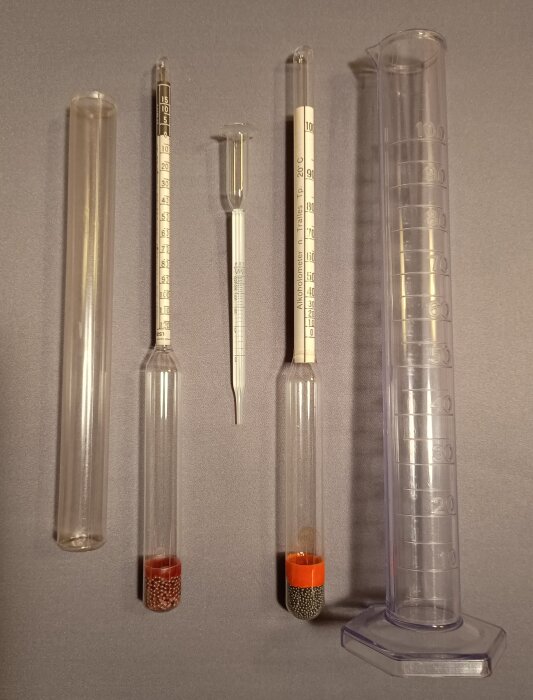 Alkoholmätare och mätcylinder för hembryggning av vin, inklusive mätinstrument med kapillärrör och olika viktmätare.