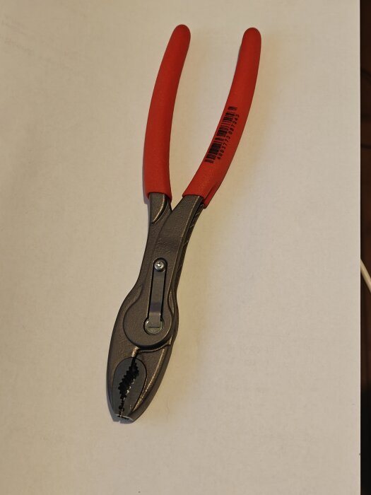 Tång med röda handtag där ena käftens kant verkar slipad ojämnt och ser tunnare ut på den högra sidan av spetsen.