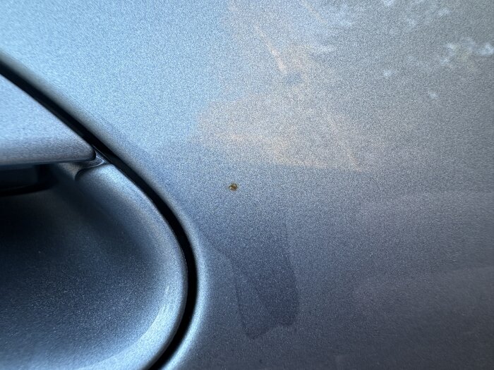 Blå bilkaross med liten brun fläck som misstänks vara flygrost nära handtaget.