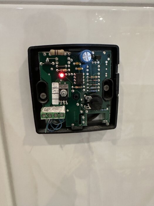 Närbild av en öppen termostat till golvvärmesystemet, visar kretskort med komponenter och en lysande röd lampa.