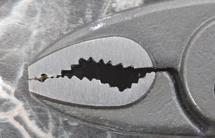 Närbild av en tångs käftar med ojämnt centrerade tänder, vilket antyder bristande kvalitetskontroll.