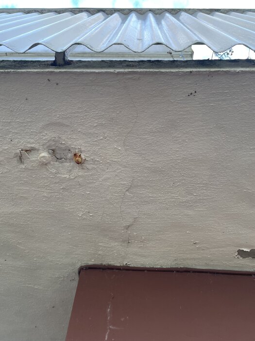Spricka i undersidan av ett betongbalkonggolv, under ett korrugerat plasttak. Ytan visar tecken på slitage och mindre skador.