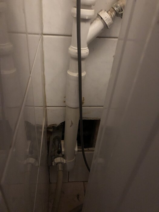 Rörsystem och vattenlås bakom tvättmaskin i ett litet rum med kaklade väggar, exponerade rör och avloppskopplingar.