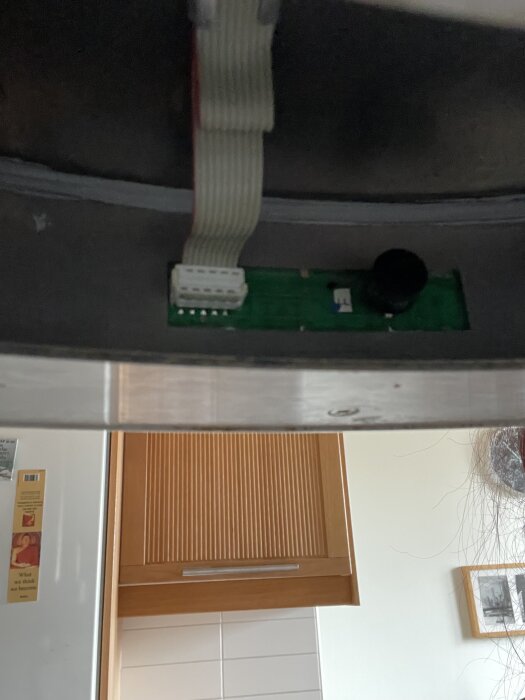 Närbild av en mekanisk fläkts trasiga kretskort från 2004, med synlig kabel, installerad i ett kök.