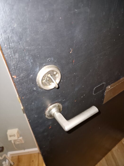 Mattsvart målad ytterdörr med silverfärgat dörrhandtag och lås, insidan visar röda färgrester.