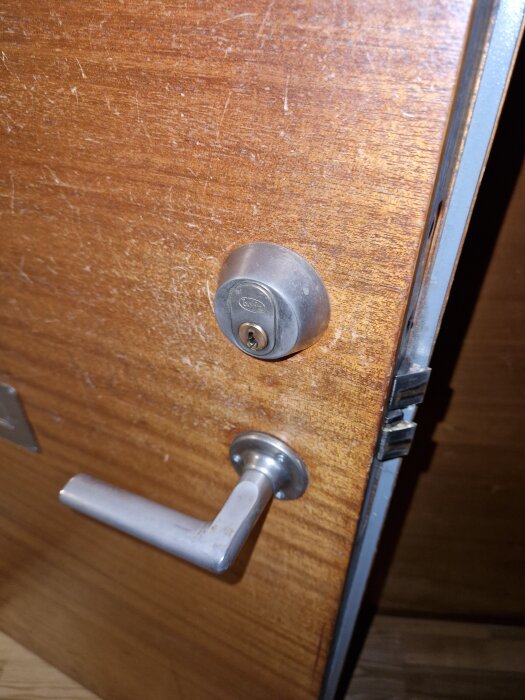 Omålad träytterdörr med metallhandtag och lås, fotograferad i närbild. Dörrens naturliga träfärg och mönster är synligt.