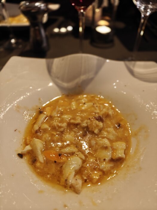 Ravioli med tryffel i sås, serverad på en vit tallrik. Bakom finns vinglas och bordsmiljö, vilket antyder en fin middag.