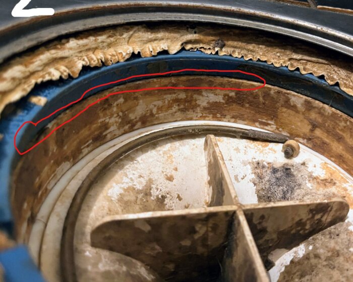 Närbild av en klämring där tätskiktet syns sticka ut i överkanten, markerat med en röd cirkel. Tecken på slitage och smuts är synliga.