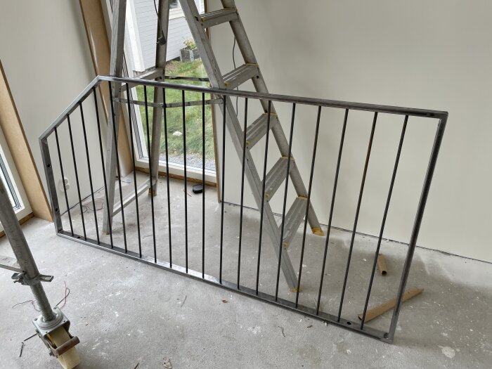 Metallräcke av 10mm rundstång och 40x20x2 profil, lutad mot en vägg inuti ett rum, bredvid en stege och ett fönster.