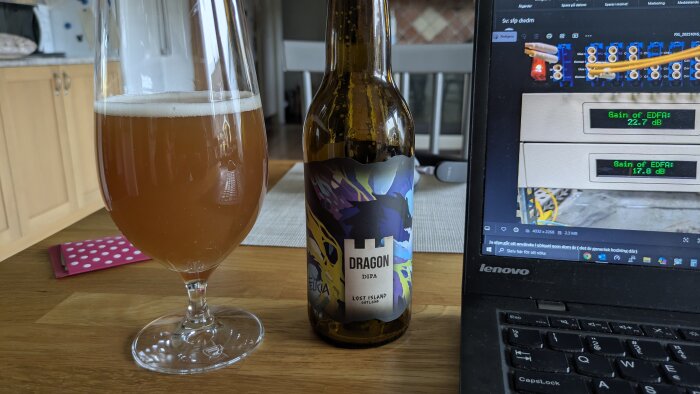 Flaska Dragon Dipa-öl från Gotland och ett halvfullt glas på ett bord bredvid en laptop.