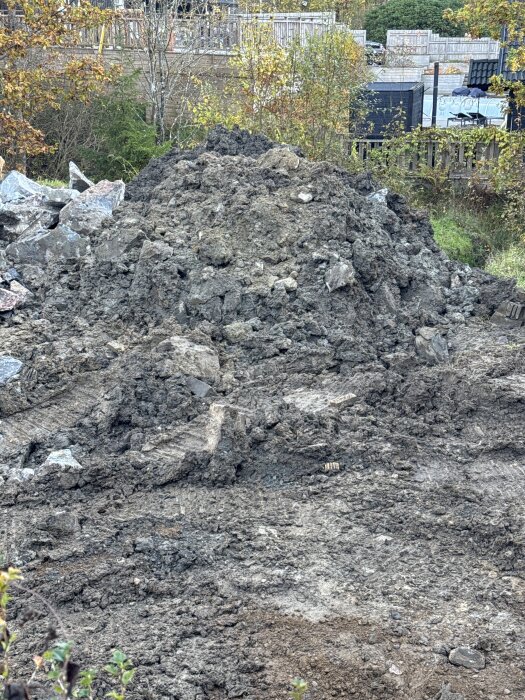 Hög med jord och sten vid en byggarbetsplats i Nödinge, omgiven av höstfärgade träd och staket i bakgrunden.