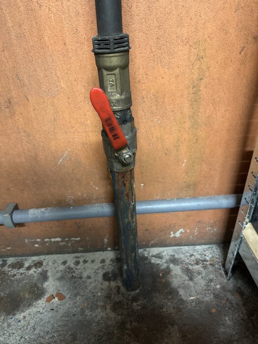 Inkommande vattenrör med ventil i ett hus, mot en orange vägg, med misstänkt doft av bensin i vattnet.