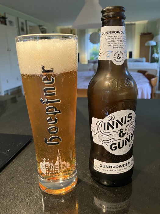 Glas med öl från Hoegaarden bredvid en flaska Innis & Gunn Gunnpowder IPA på ett köksbord i hemtrevlig miljö.