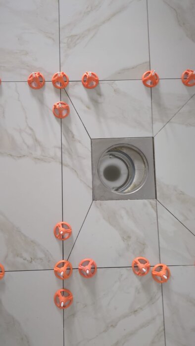 Klinkergolv runt golvbrunn med synlig tätskikt, orange plastbrickor synliga mellan plattorna.