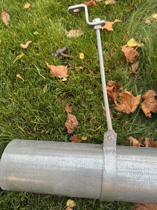 Metallrör med metallfäste och gängad stång liggande på gräs med höstlöv.