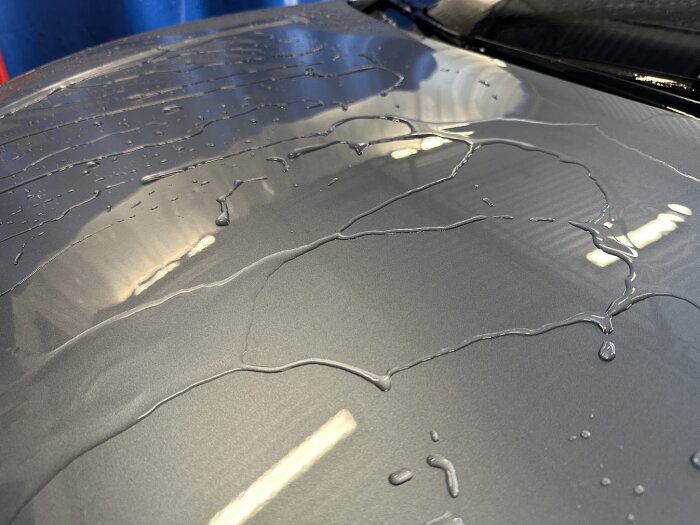Vatten på motorhuv efter biltvätt, med god avrinning av droppar synlig, vilket indikerar effektiv användning av rengöringsprodukt.