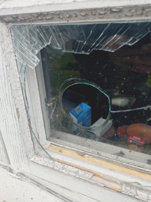 Trasigt fönster med ett runt hål, sprucket glas runt omkring, låscylinderproblem för garageport beskrivs i inlägg.